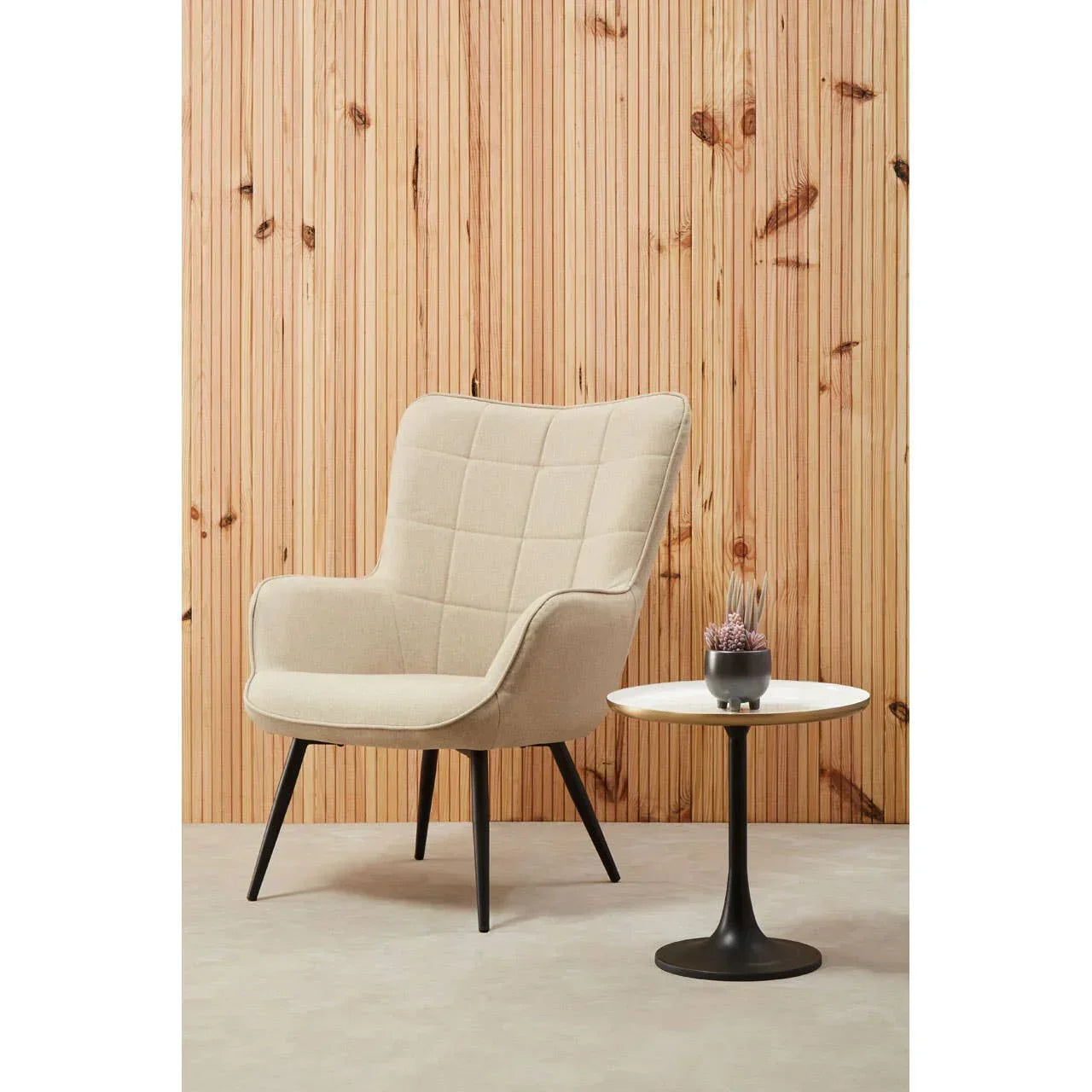 Beige accent armchair with black legs beside round side table on modern wood panel wall