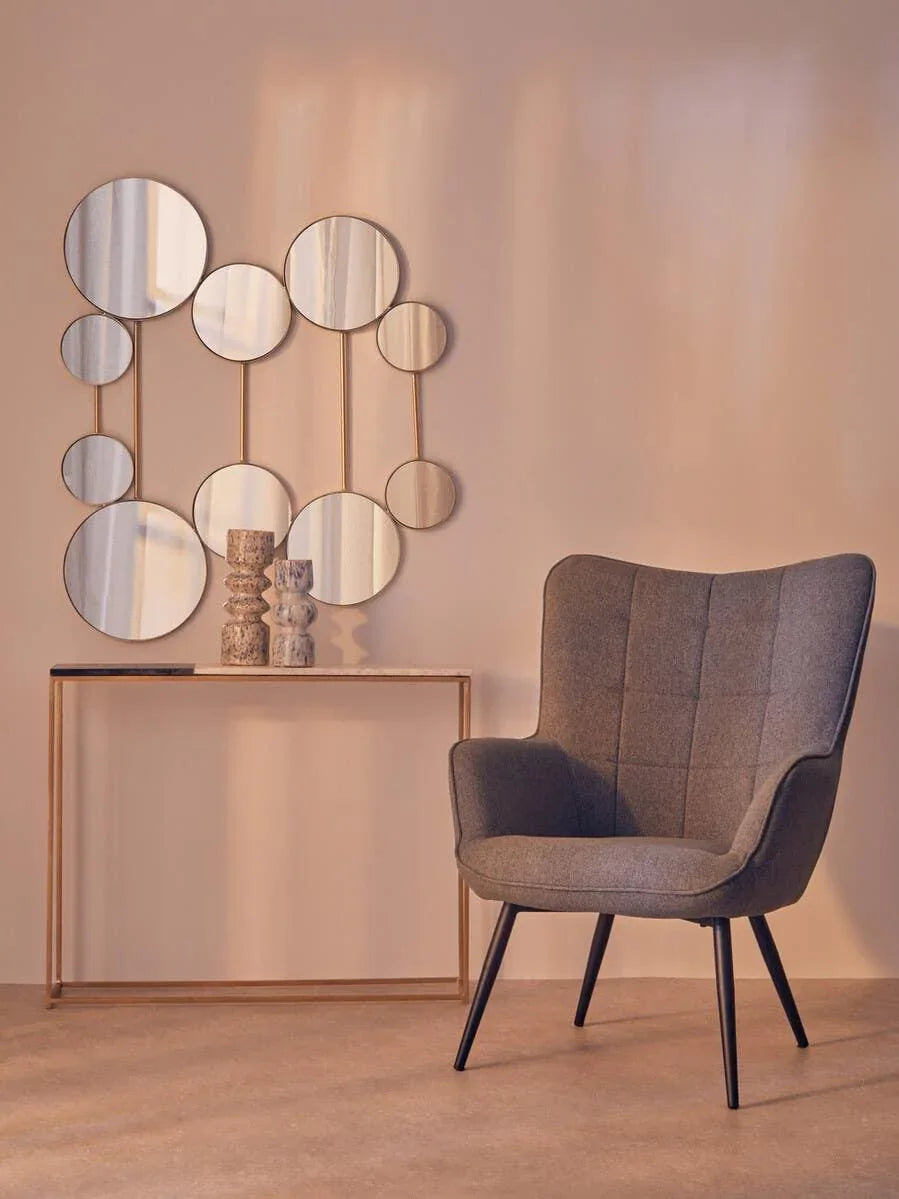 Modern accent chair with grey upholstery beside gold console table and geometric wall mirror