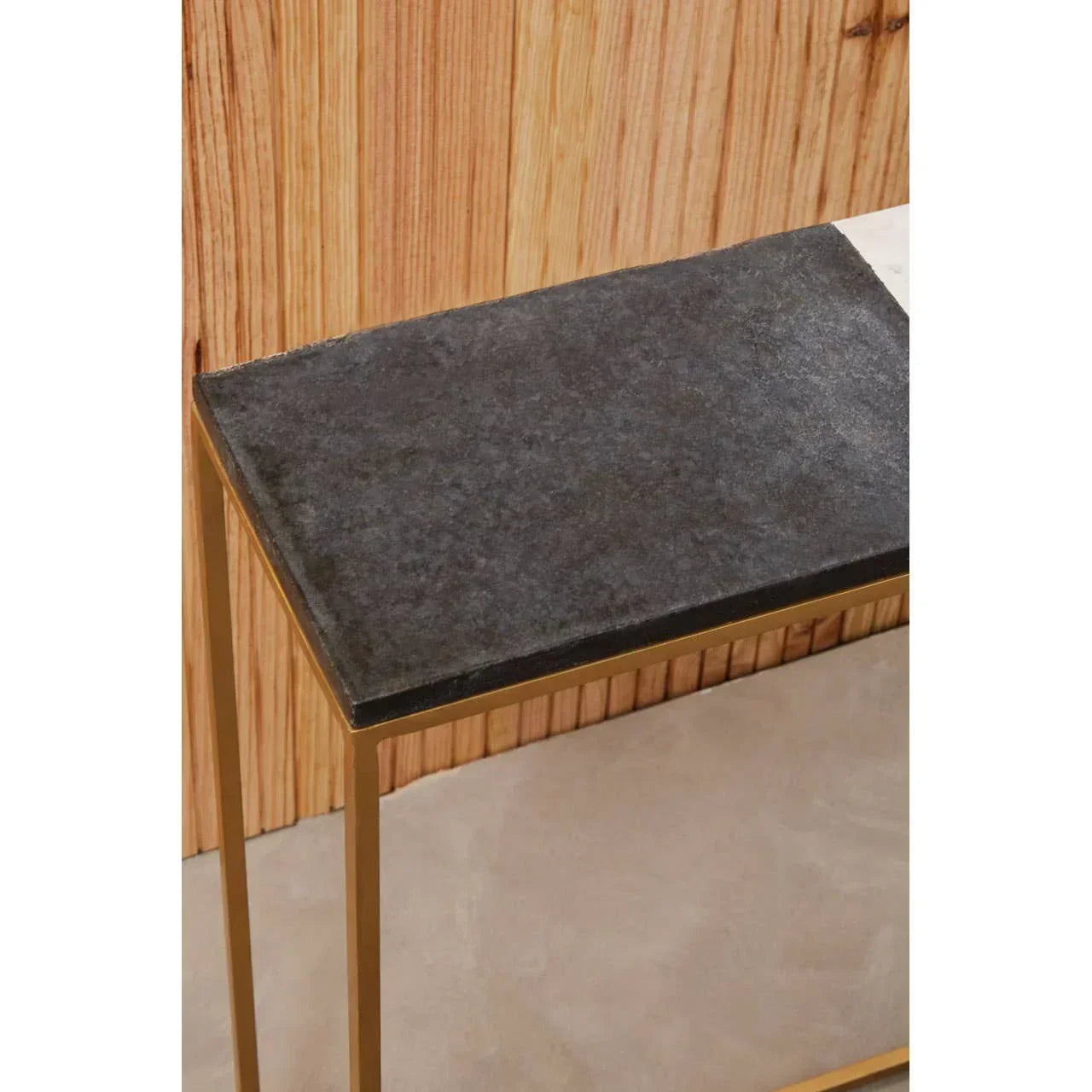 Console table with black stone top and gold metal frame against wood panel wall