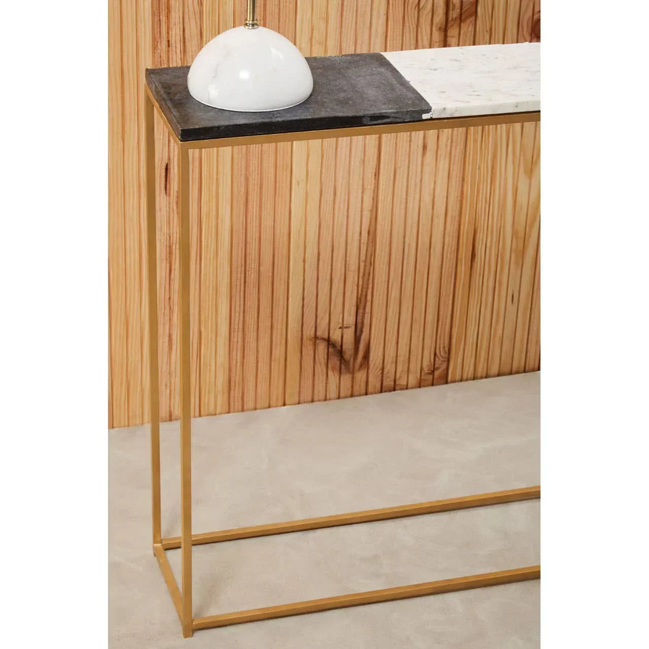 Marble console table with gold metal legs and black stone accent against wood panel wall