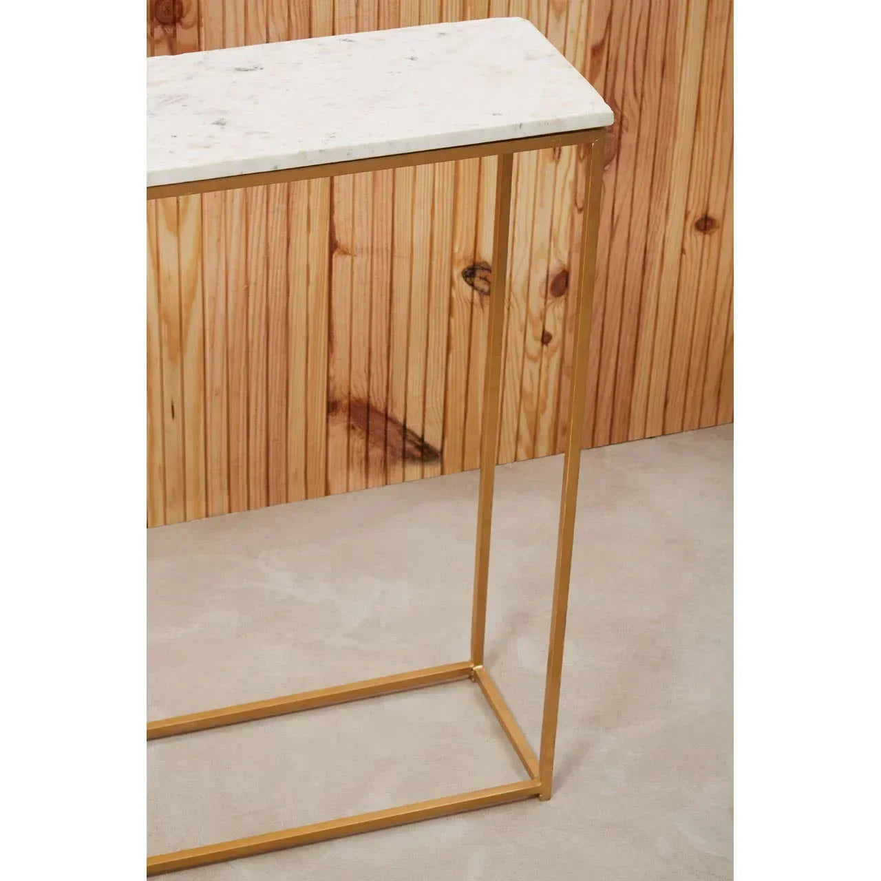 White marble console table with slim gold metal frame against wood panel wall
