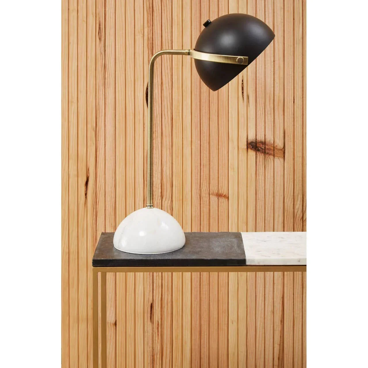 Black and gold desk lamp with white marble base on console table against wood panel wall