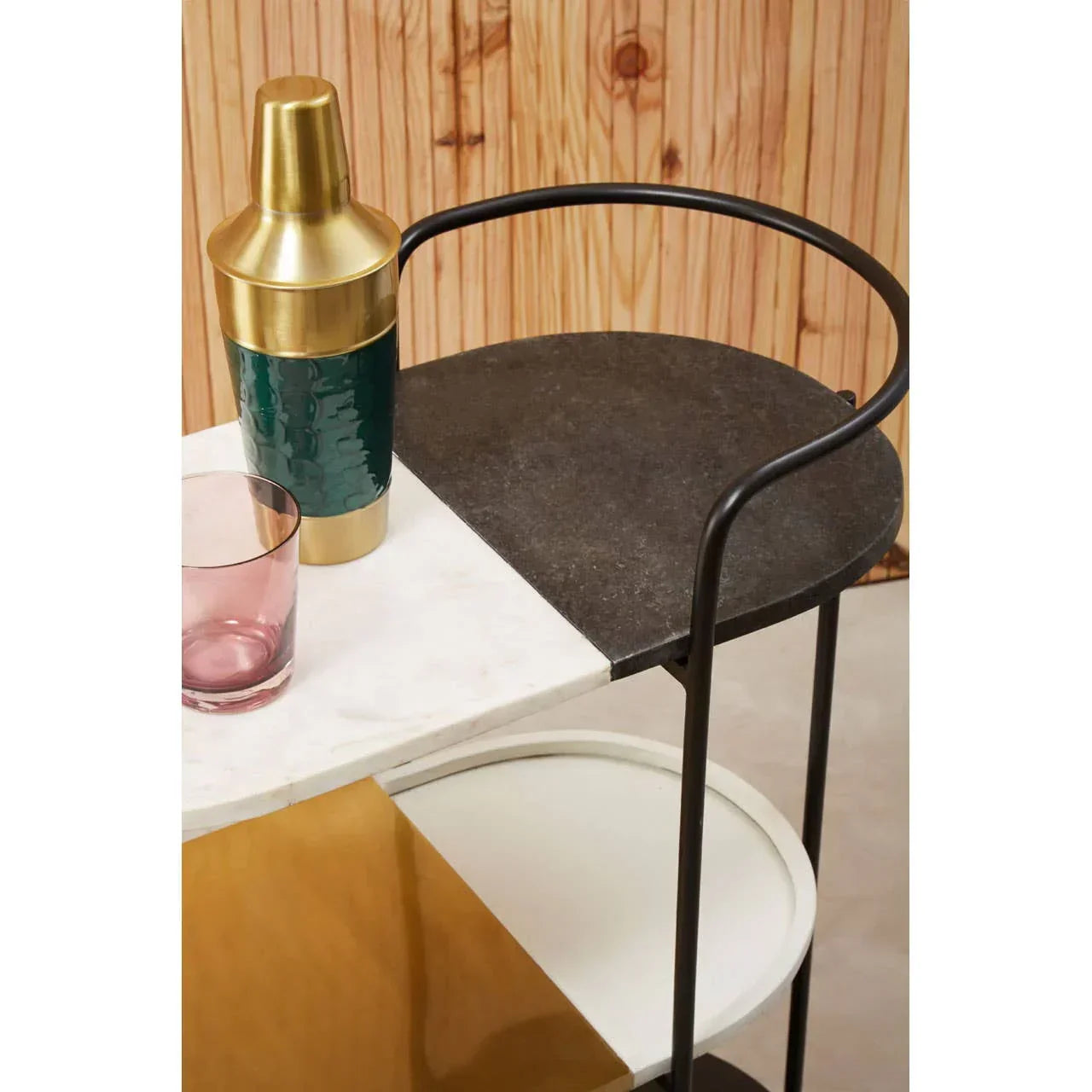 Three-tier bar cart with black frame, mixed stone shelves, cocktail shaker and glass