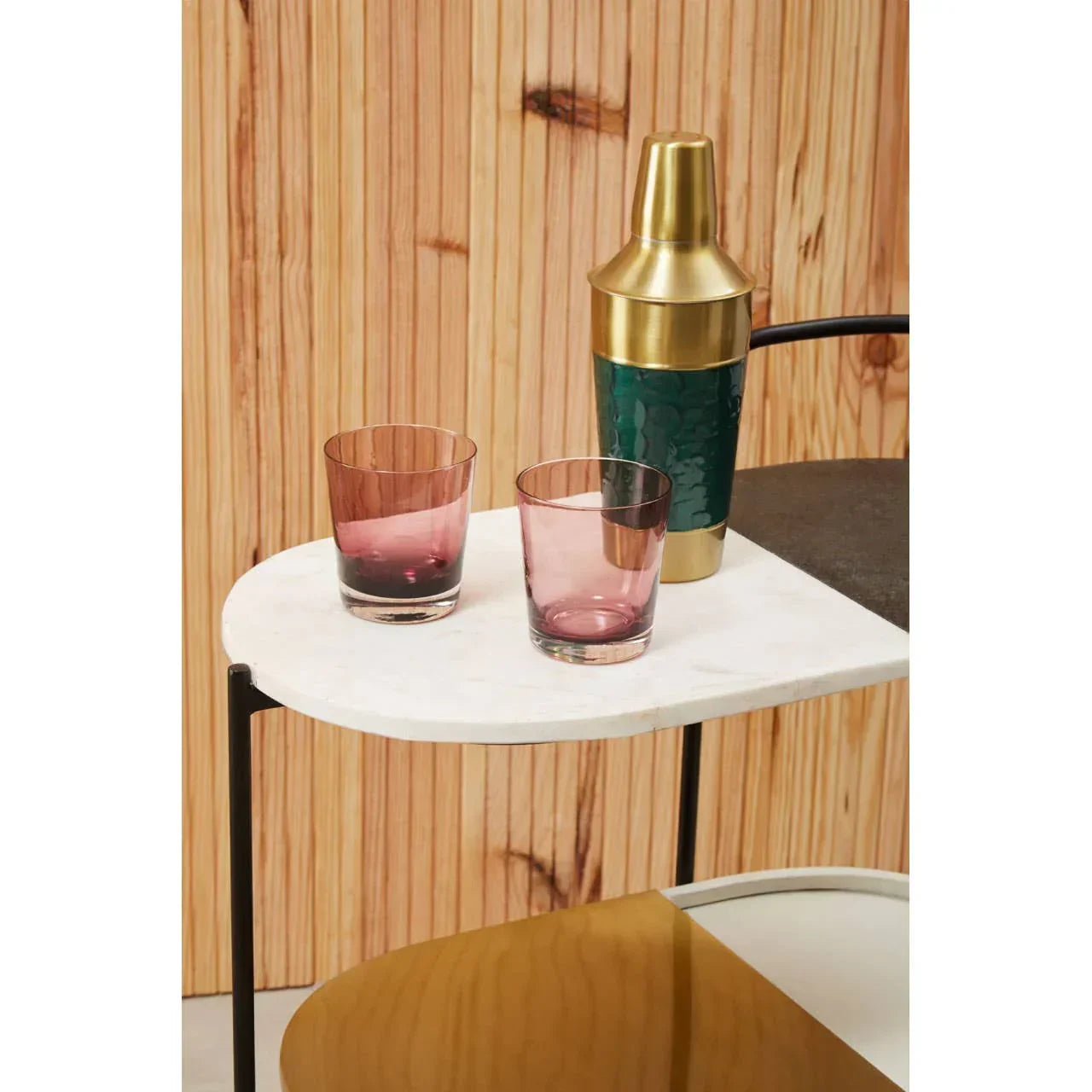 Two purple glass tumblers and a gold cocktail shaker on a marble side table