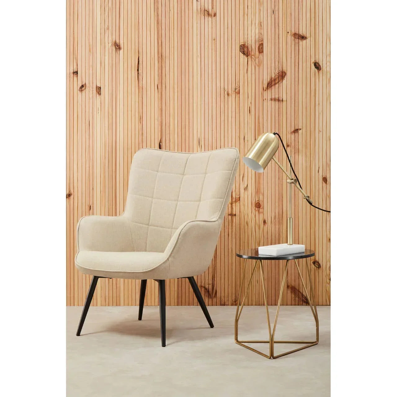 Beige upholstered accent chair with black legs beside gold side table and brass lamp