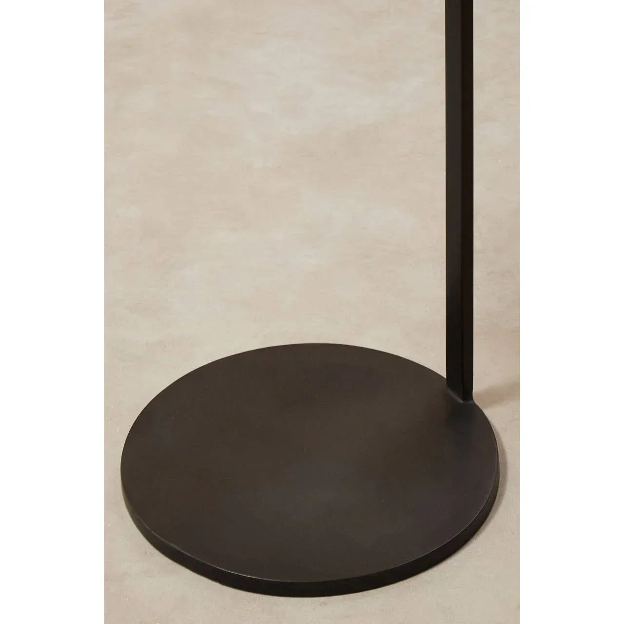 Black metal side table base on light beige floor, circular with minimalist design
