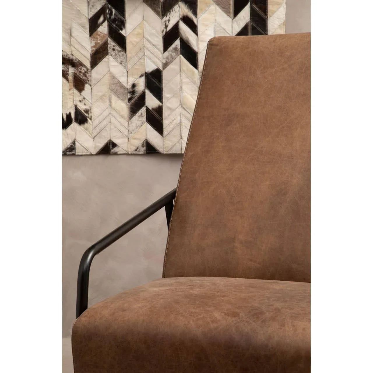 Brown leather armchair with black metal armrest, geometric wall art in background