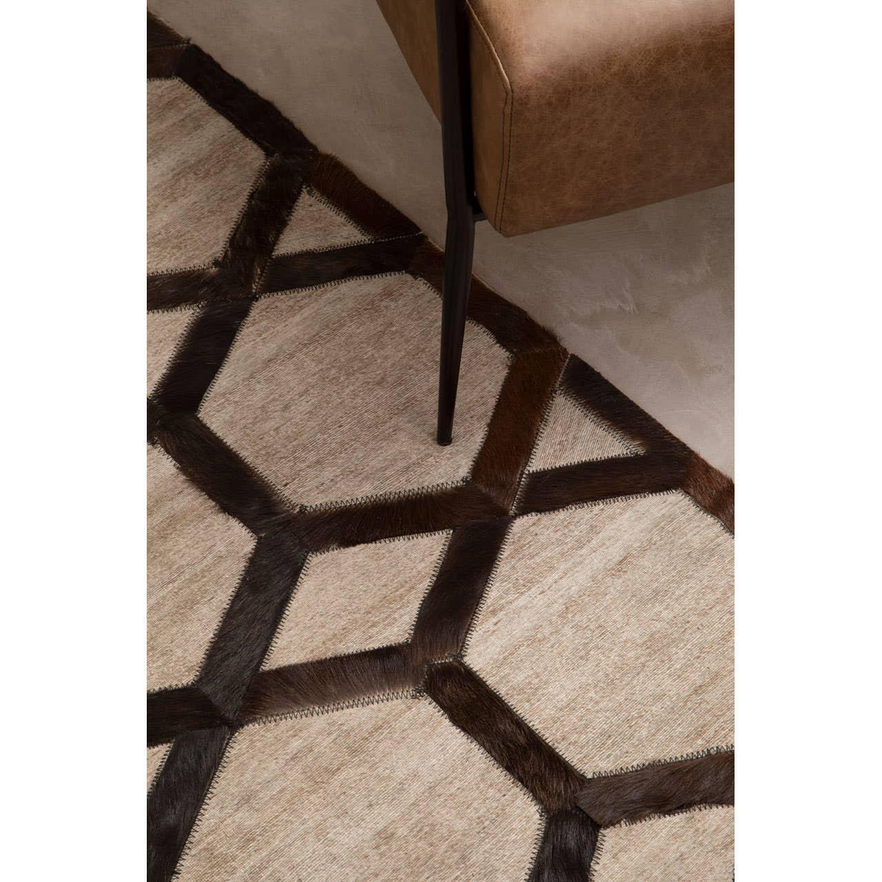 Geometric patterned rug with brown hexagons and tan sections beside leather sofa leg