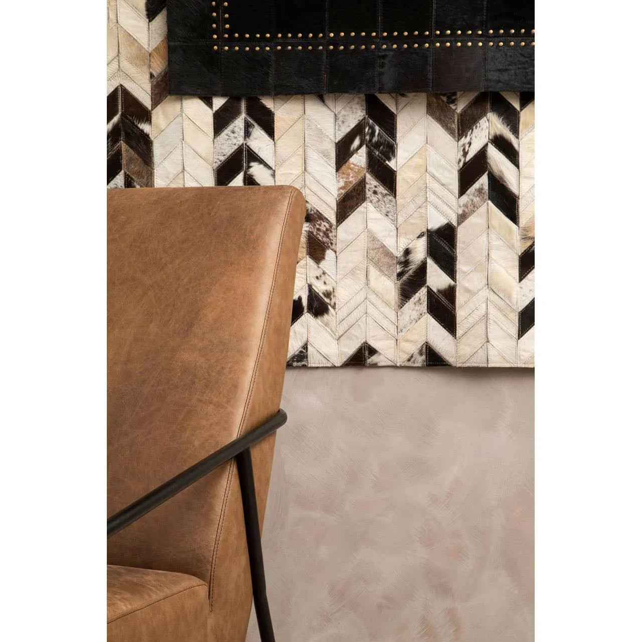 Brown leather armchair with black metal armrest in front of chevron wall panel