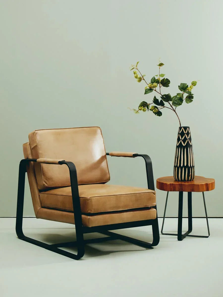 Tan leather armchair with black metal frame beside wooden side table and decorative vase