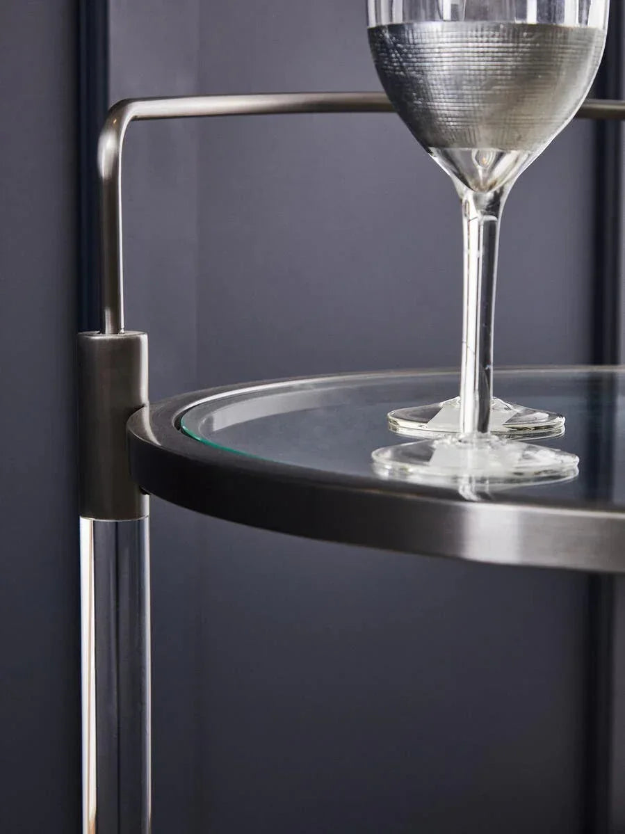Modern glass and metal bar cart with a wine glass on top shelf, close-up view