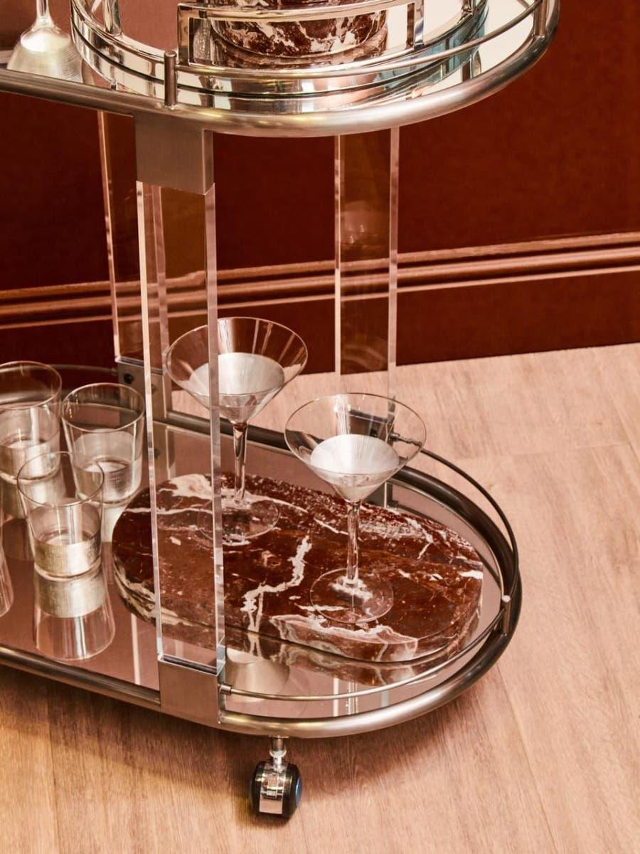 Modern drinks trolley with chrome frame, marble shelf, and glassware on wood floor