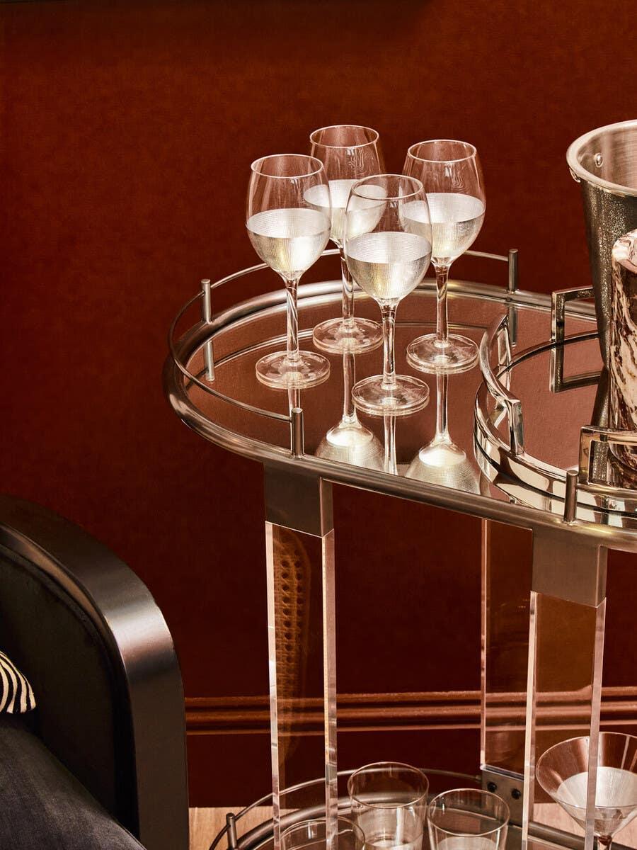 Glass drinks trolley with chrome trim, holding wine glasses and ice bucket against red wall