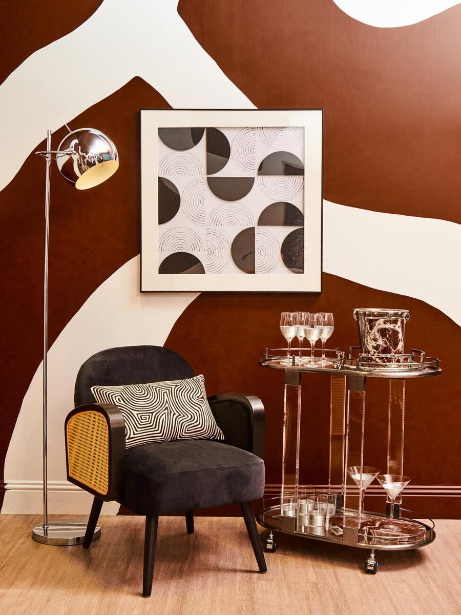 Black accent chair with cane arms, bar cart with glassware, geometric wall art and lamp