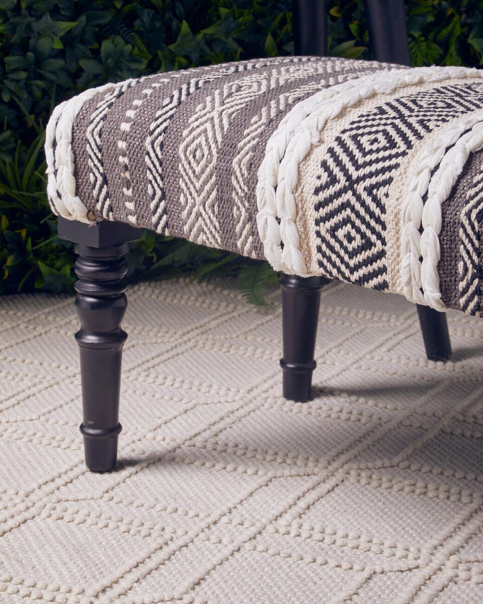 Patterned upholstered bench with dark wooden legs on textured cream rug