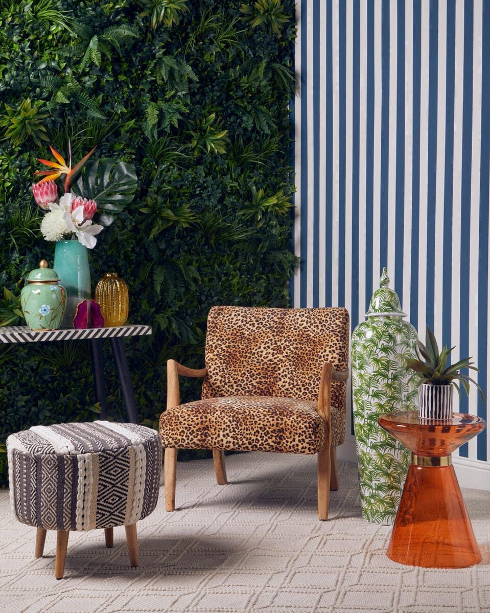 Leopard print accent chair with wooden arms, patterned ottoman, and orange side table in living room