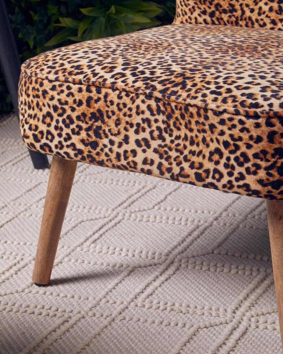 Leopard print accent chair with wooden legs on textured cream rug