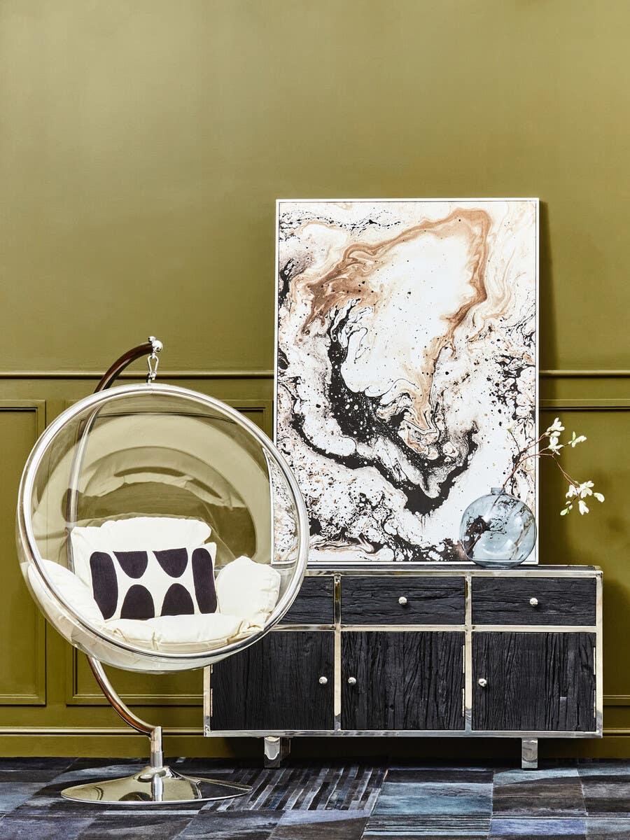 Modern bubble chair with cushion beside black wood sideboard and abstract art panel