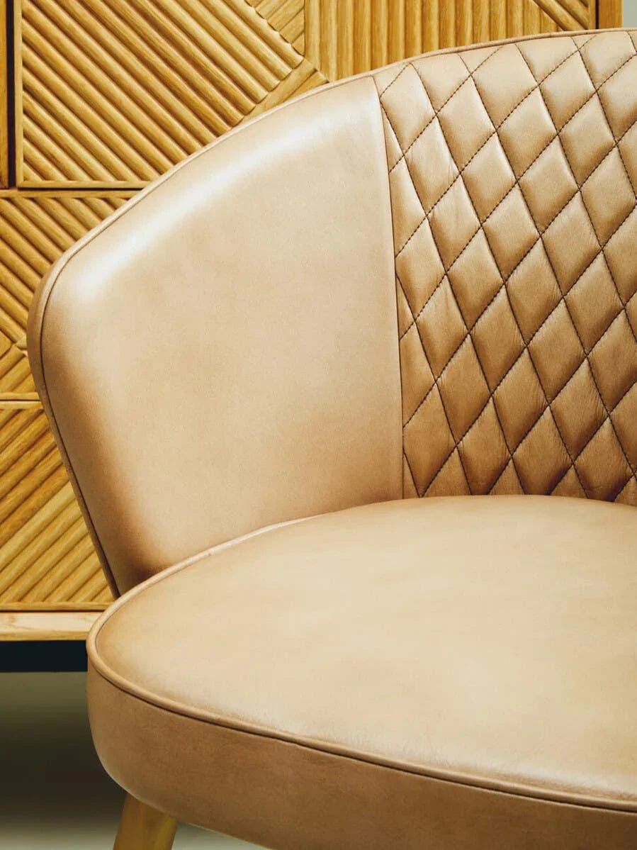 Tan leather accent chair with quilted backrest next to wooden textured cabinet
