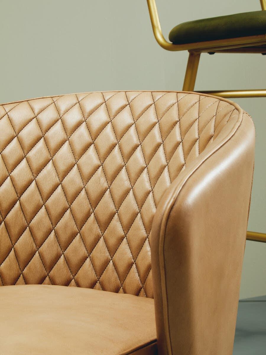 Tan leather armchair with quilted backrest and curved arm in modern interior setting