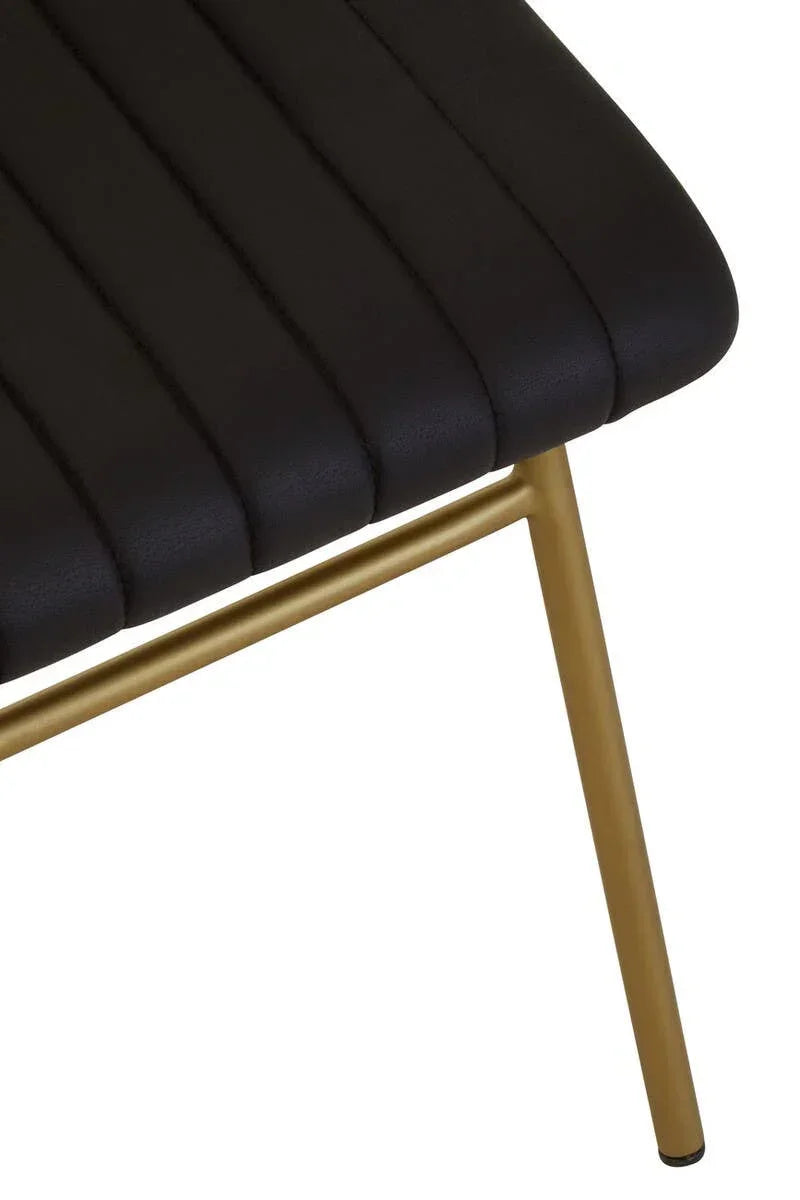 Close-up of black upholstered dining chair seat with gold metal legs