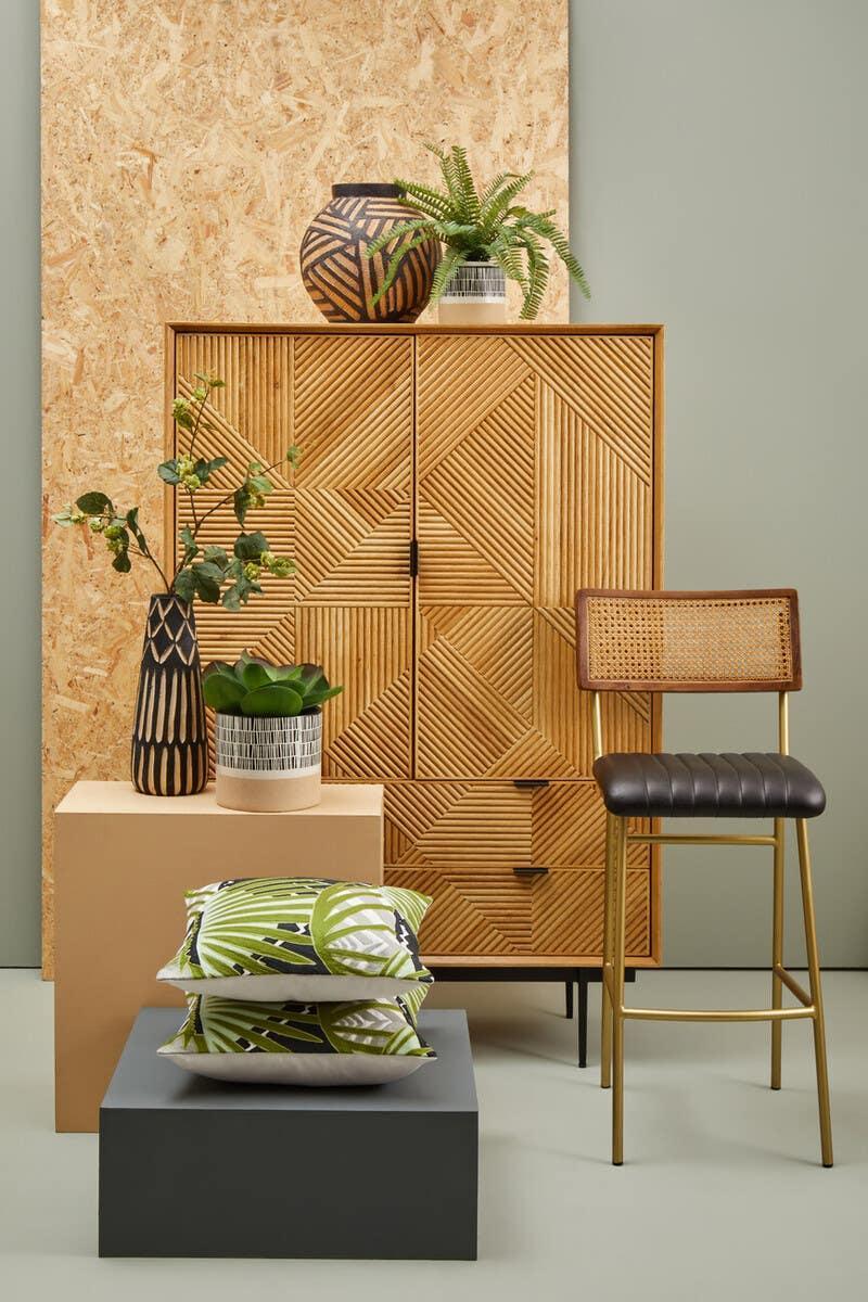 Geometric wood cabinet, rattan bar stool, green leaf cushions, and modern decorative vases