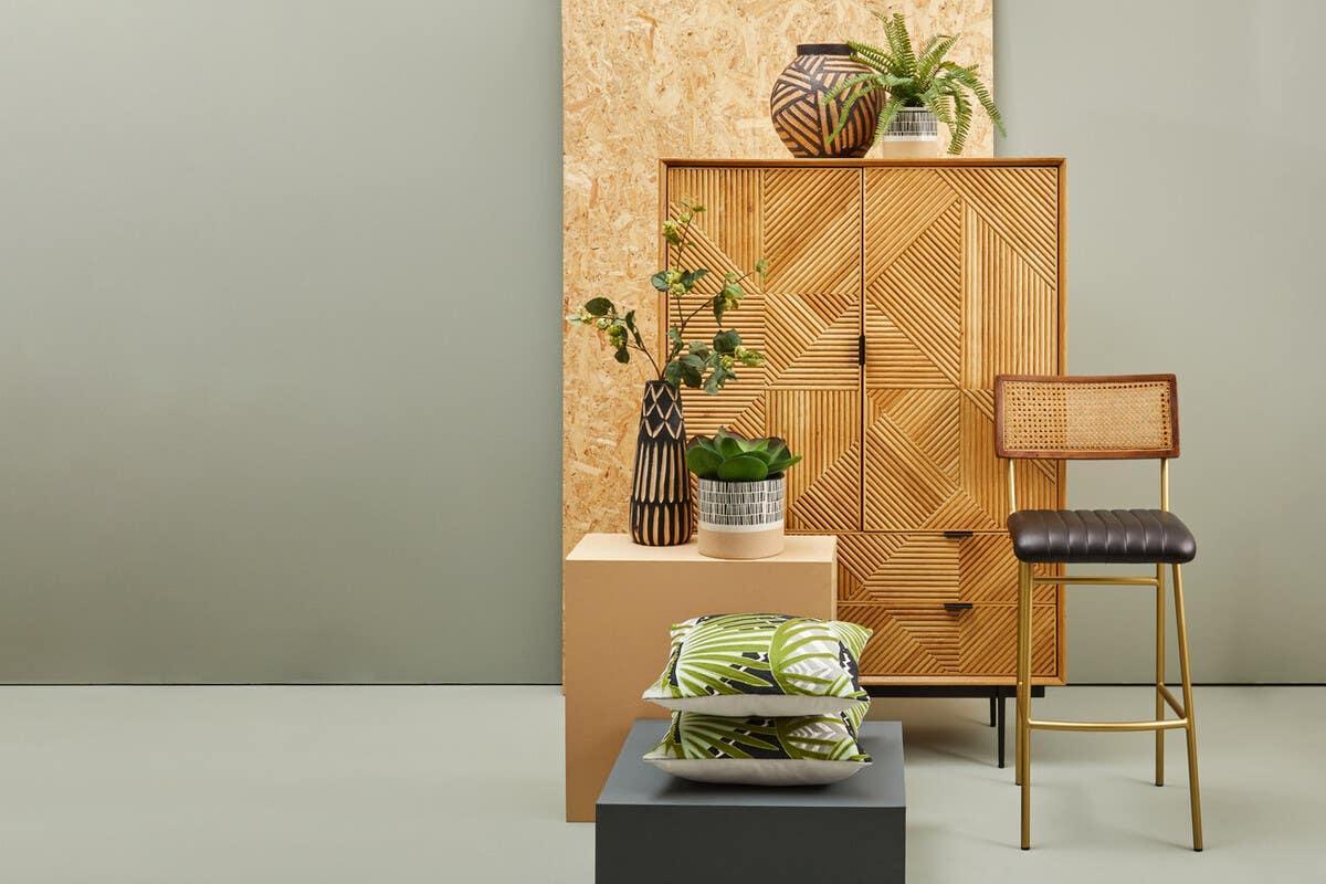 Geometric wood sideboard with rattan bar stool, indoor plants, and cushions in modern setting