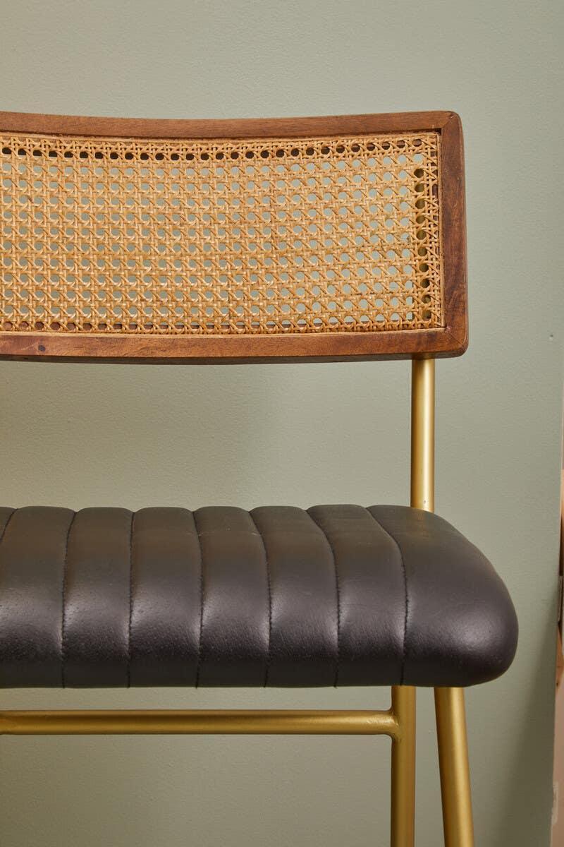 Bar stool with black faux leather seat, rattan backrest, and gold metal frame