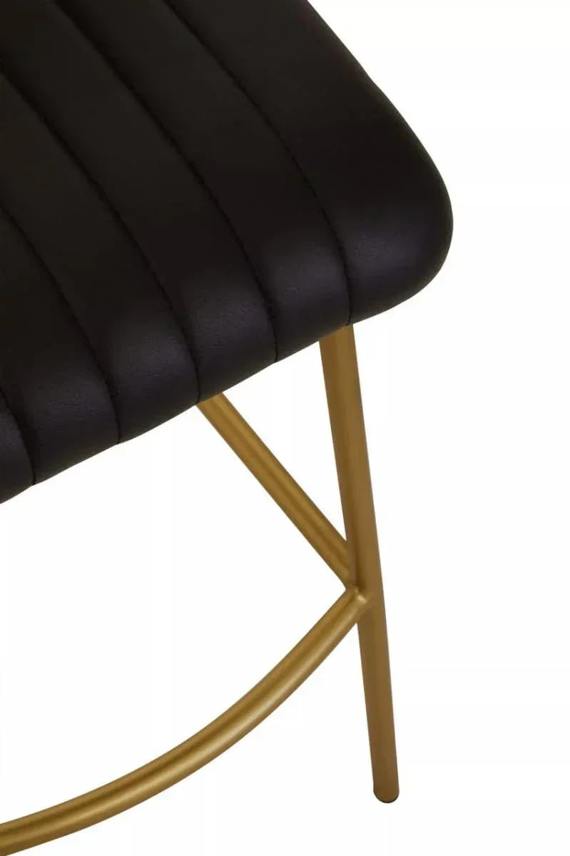 Black leather dining chair seat with gold metal legs, close-up view