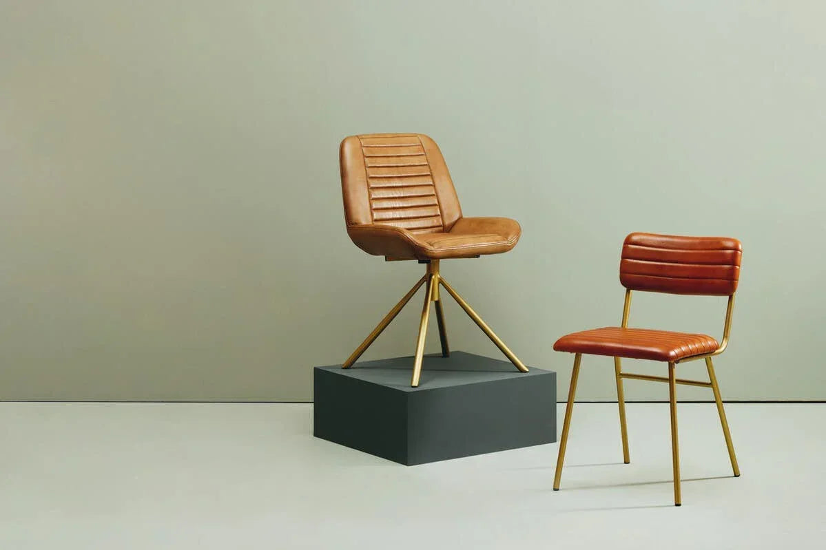 Tan leather dining chairs with gold metal legs, one on pedestal, against neutral background