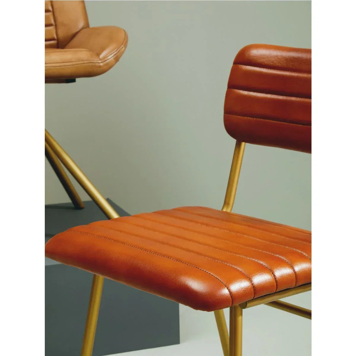 Tan leather dining chair with gold metal legs and horizontal stitched seat detail