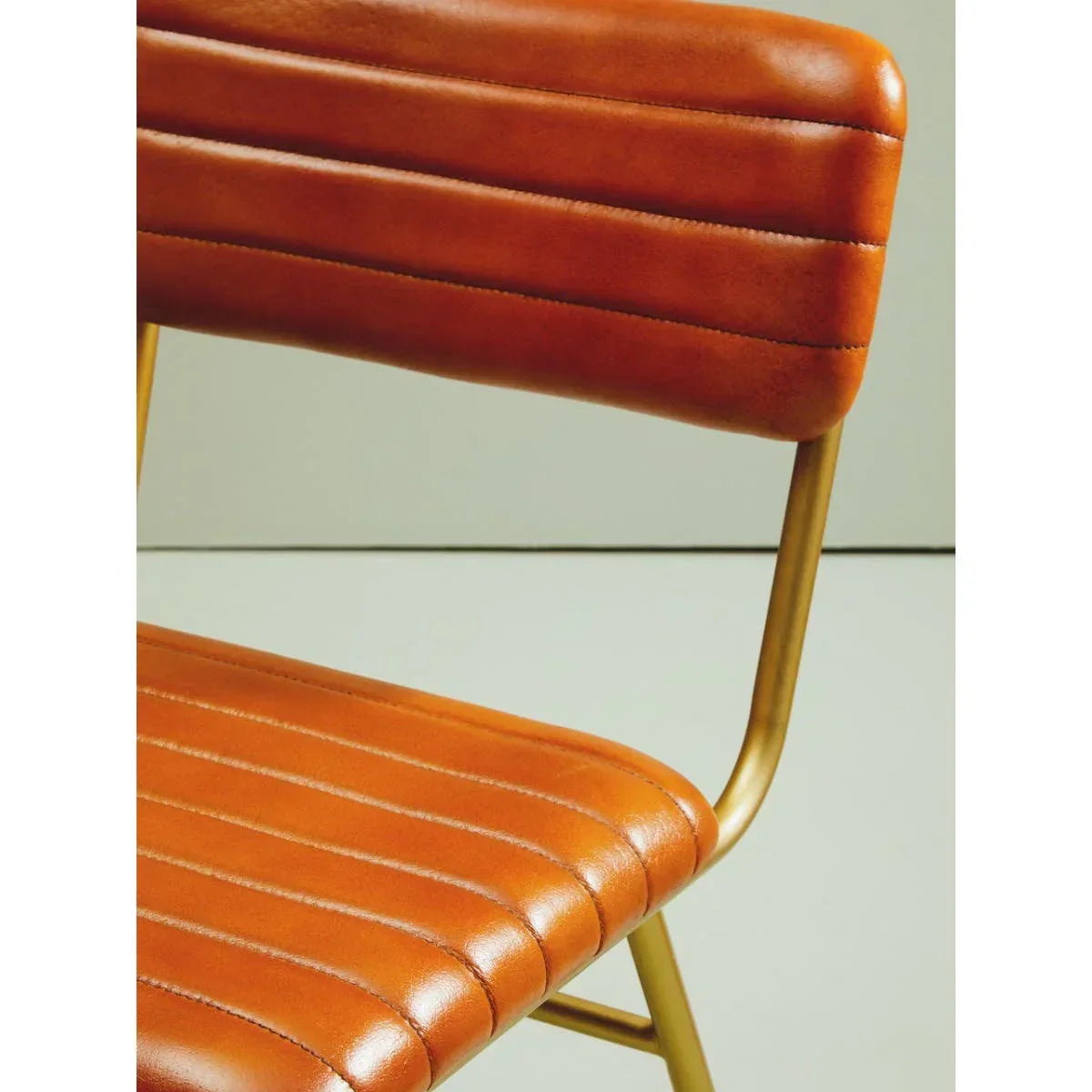 Brown leather dining chair with stitched seat and gold metal frame, side angle view