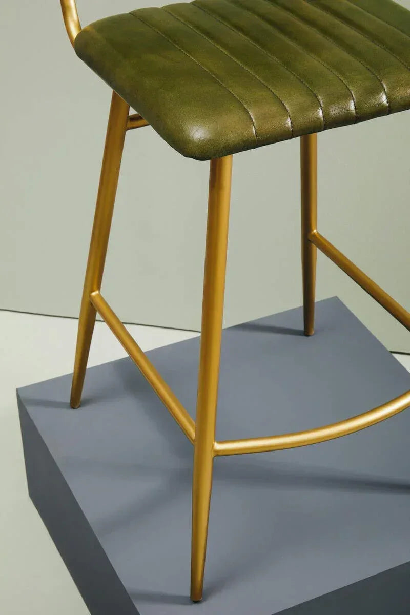 Green leather bar stool with gold metal legs on a grey platform, side angle view