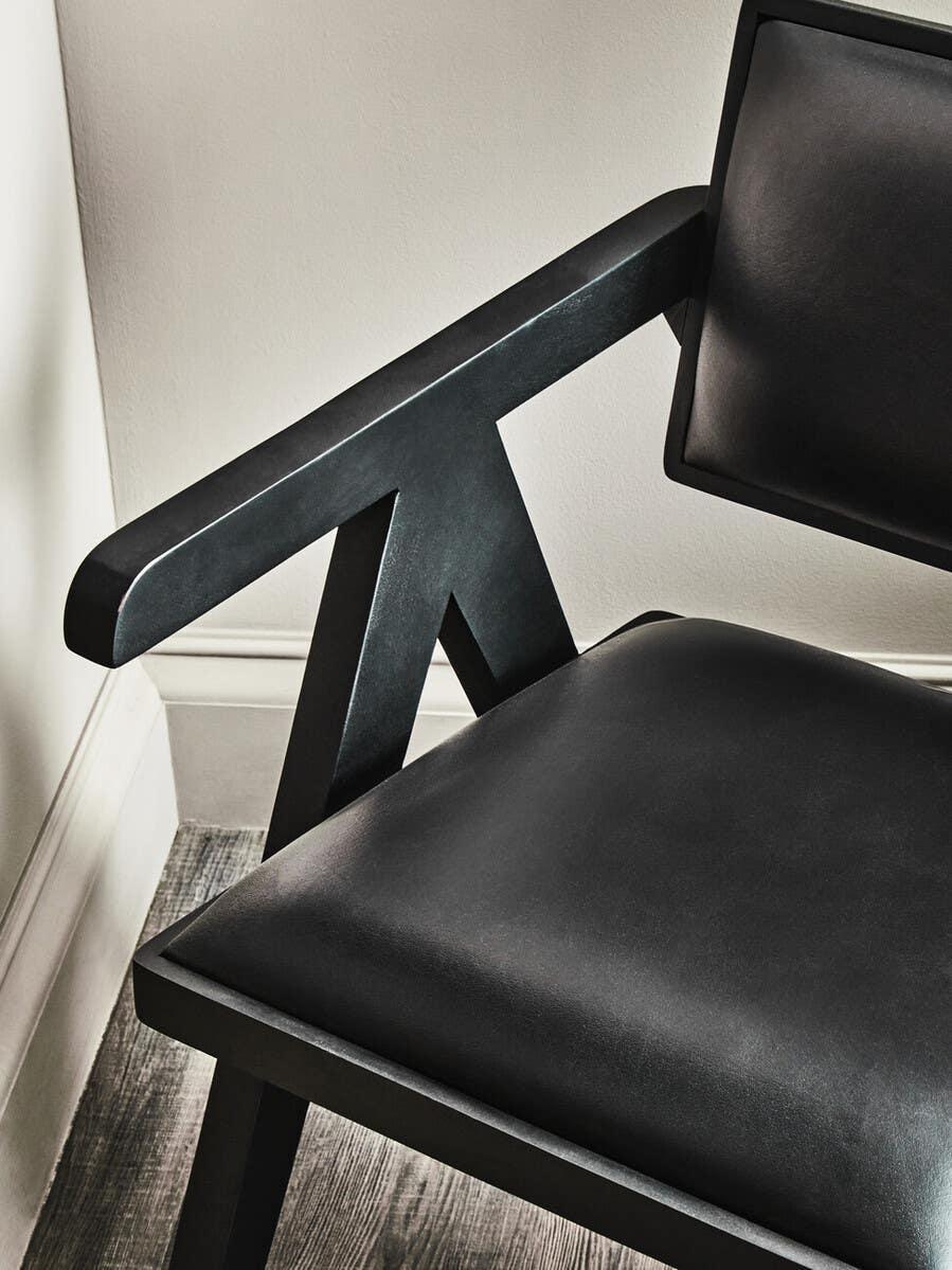 Black leather dining chair with angled armrest and cushioned seat on wood floor