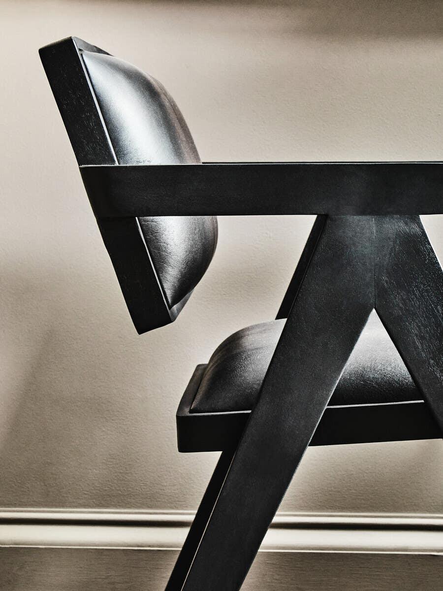 Side view of modern black leather dining chair with angled wooden frame