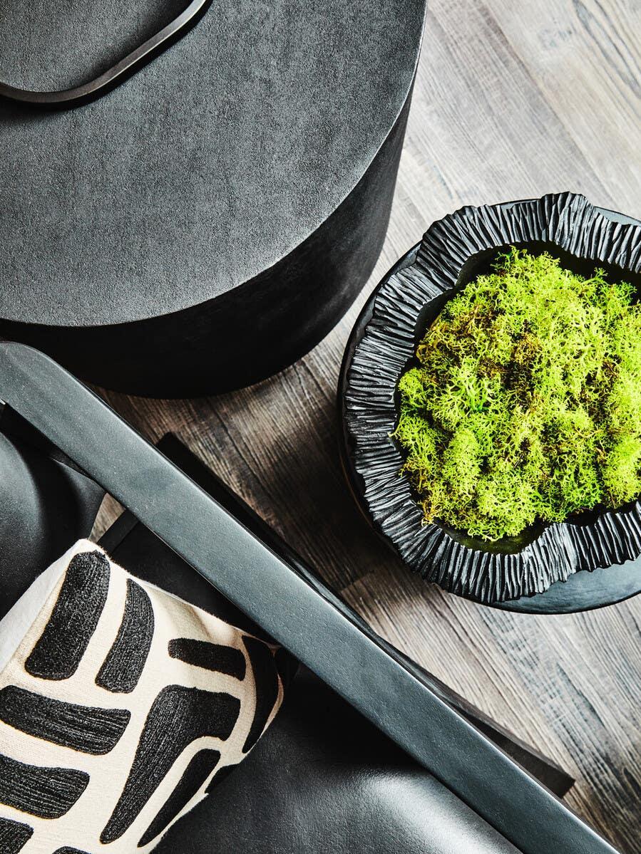 Black side table, green decorative plant, and patterned cushion on wood floor