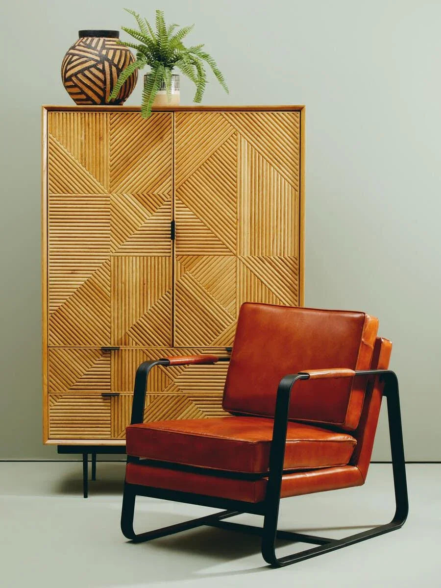 Brown leather armchair with black metal frame in front of geometric wooden cabinet