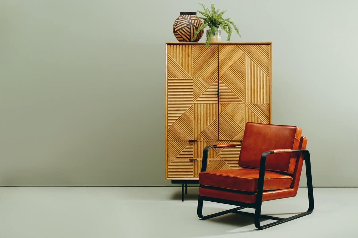 Brown leather armchair with black metal frame beside geometric wood cabinet and decor