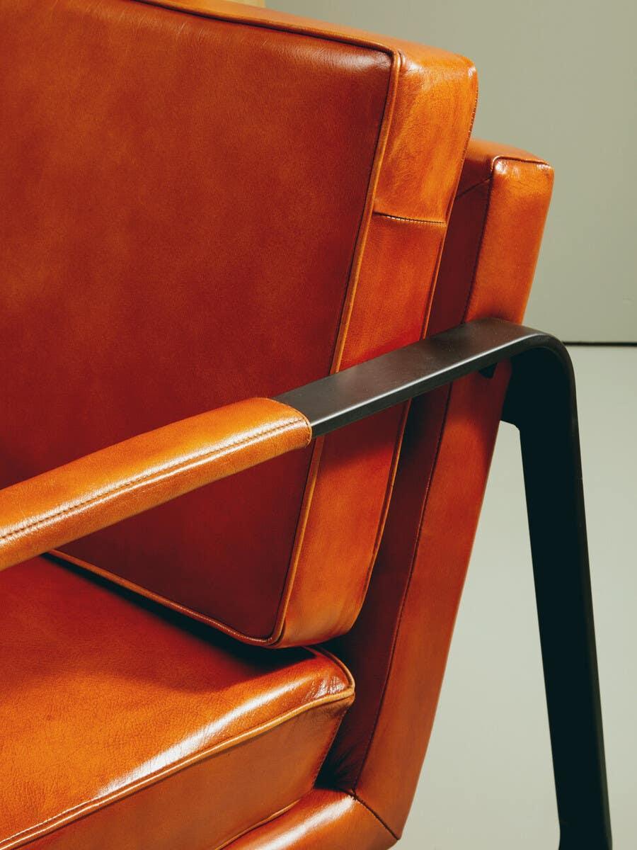 Close-up of orange leather armchair with metal armrest and stitched cushions