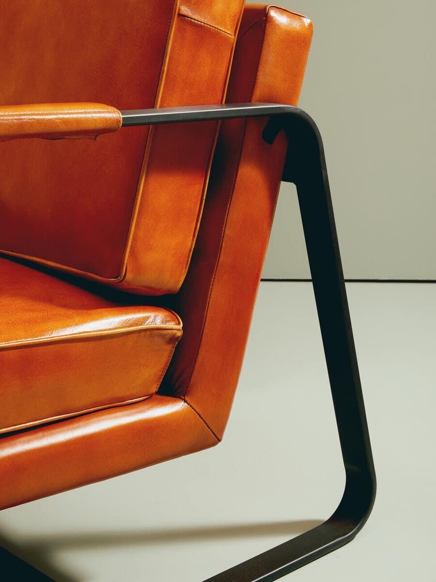 Close-up of modern leather armchair with orange cushions and black metal frame