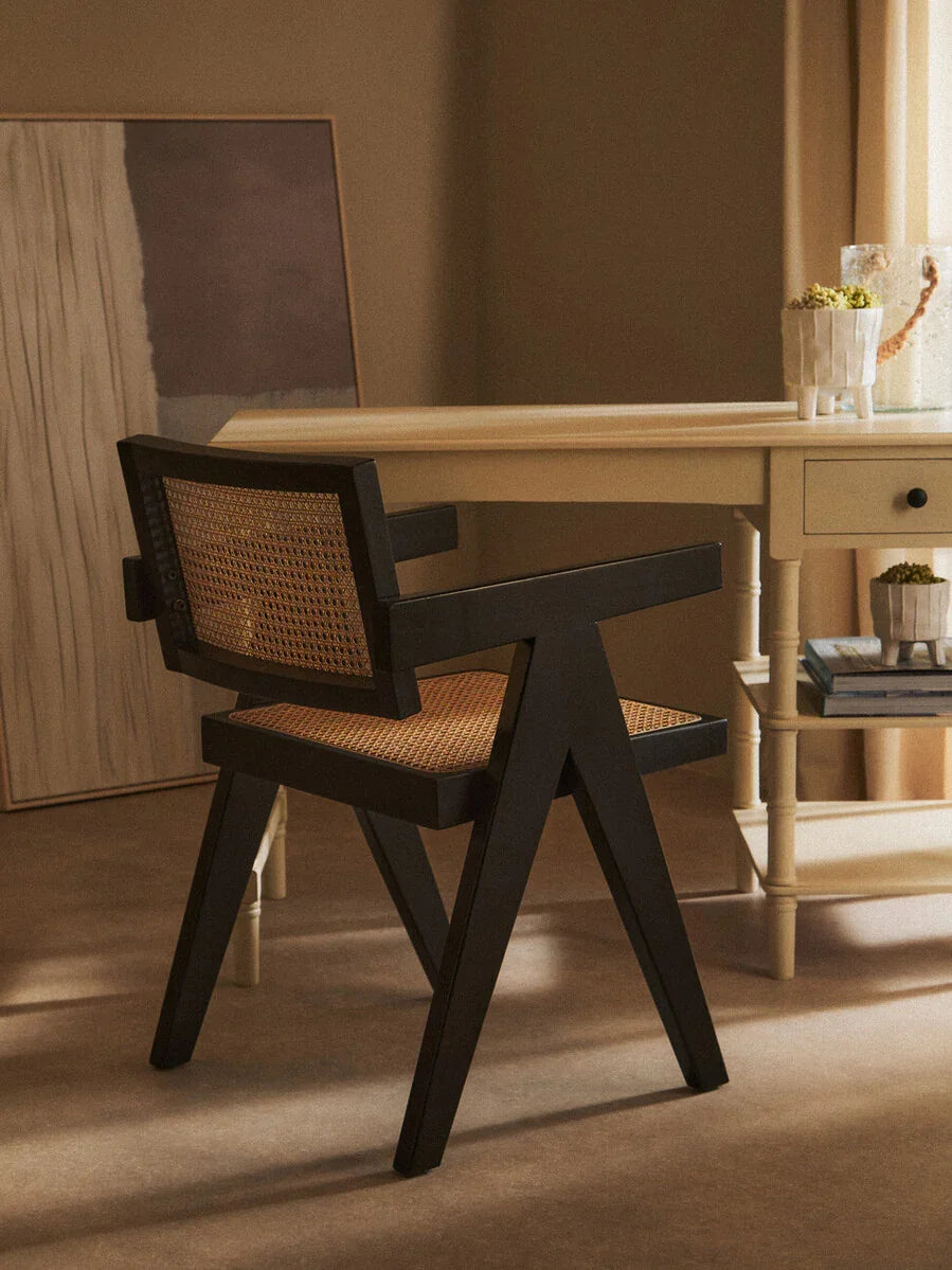 Black wooden dining chair with woven rattan seat beside cream writing desk in neutral room