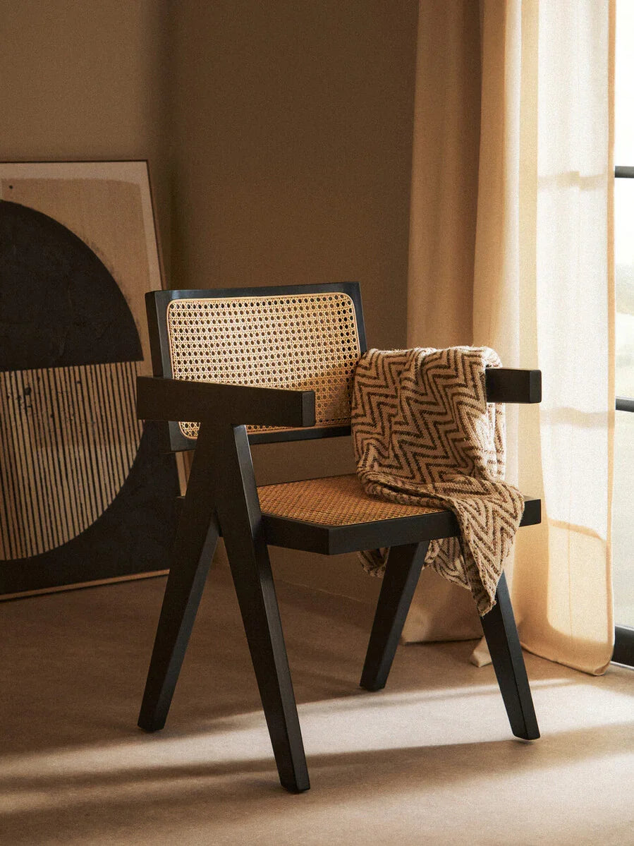Black wooden accent chair with rattan seat and back, zigzag throw draped over arm