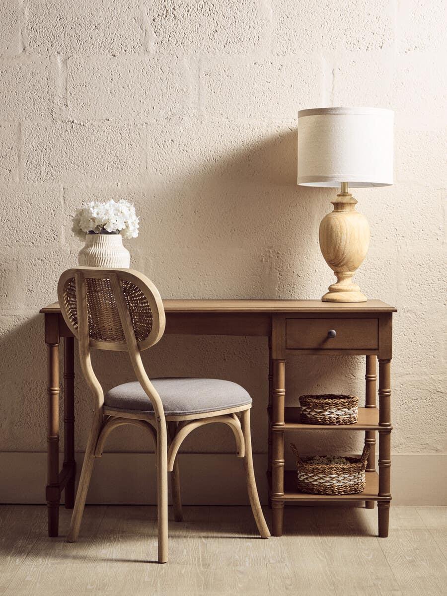 Wooden writing desk with drawer, rattan chair, table lamp and decorative vase in home office