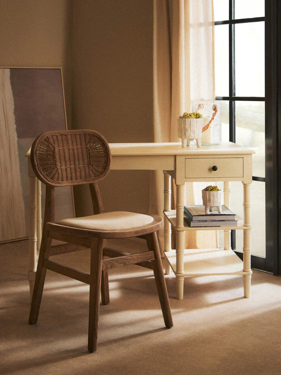 Wooden desk and rattan chair set by window with books and plant decor