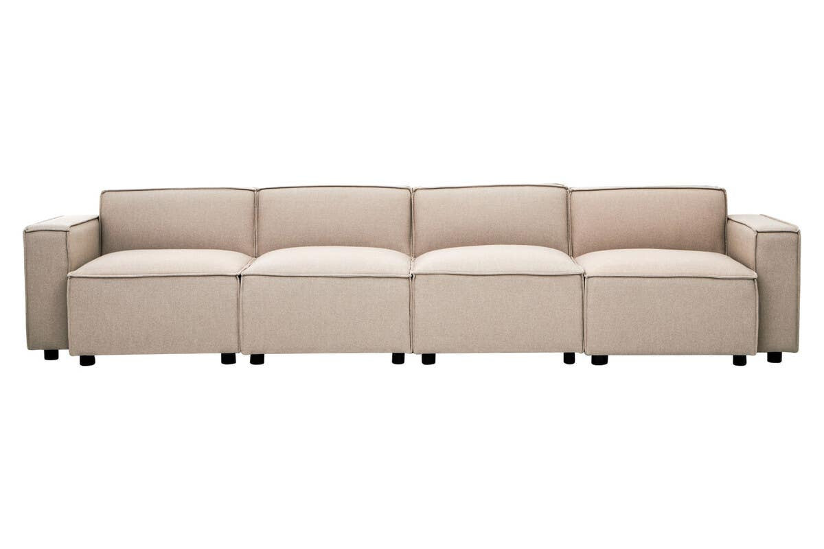 A long, armless modular sofa upholstered in natural fabric, featuring a sleek design with clean lines and a light beige color. The sofa is composed of multiple sections, each with a smooth surface and subtle stitching details, resting on small, round legs