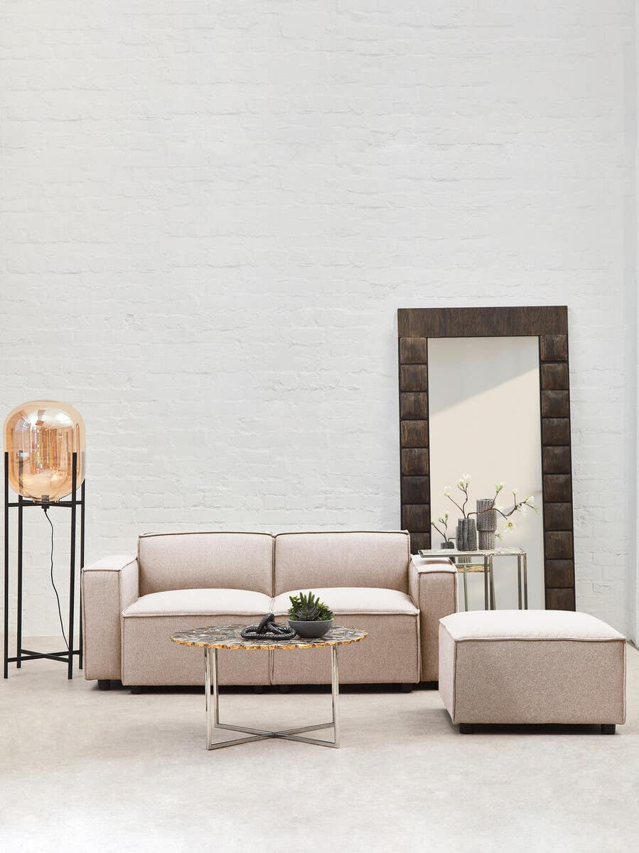 Armless modular sofa in natural fabric, featuring a light beige color, positioned in a modern living space with a large mirror and a decorative lamp on a stand. A small round table with a plant sits in front of the sofa, enhancing the contemporary aesthetic of the room. The walls are painted in a soft, neutral tone