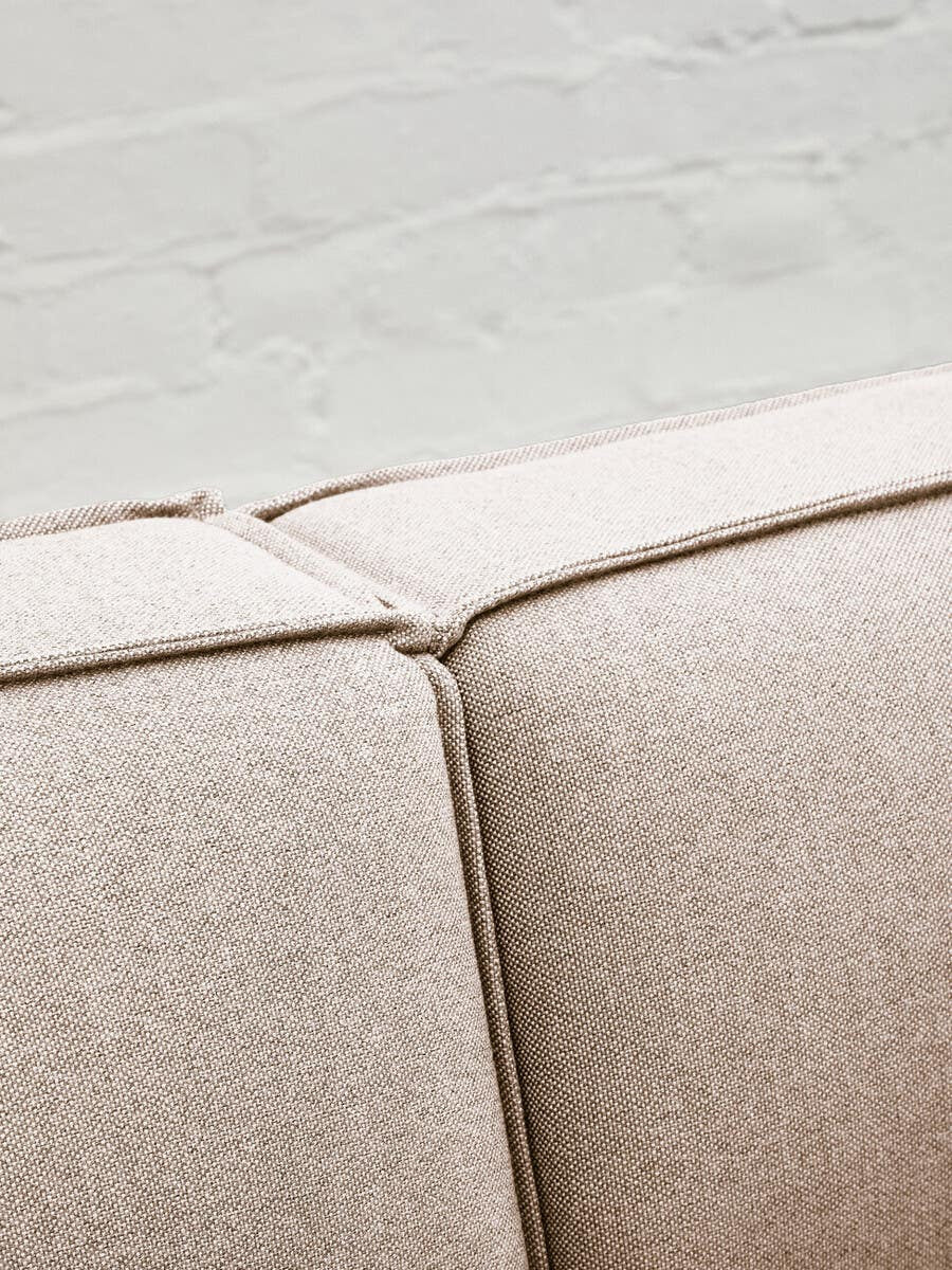 Close-up view of the Toulouse Natural Fabric Armless Modular Sofa, highlighting the soft beige fabric and the seam detail where two sections meet, set against a light-colored floor