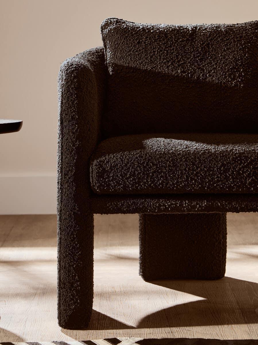 Textured black armchair with boucle upholstery on wooden floor in natural light