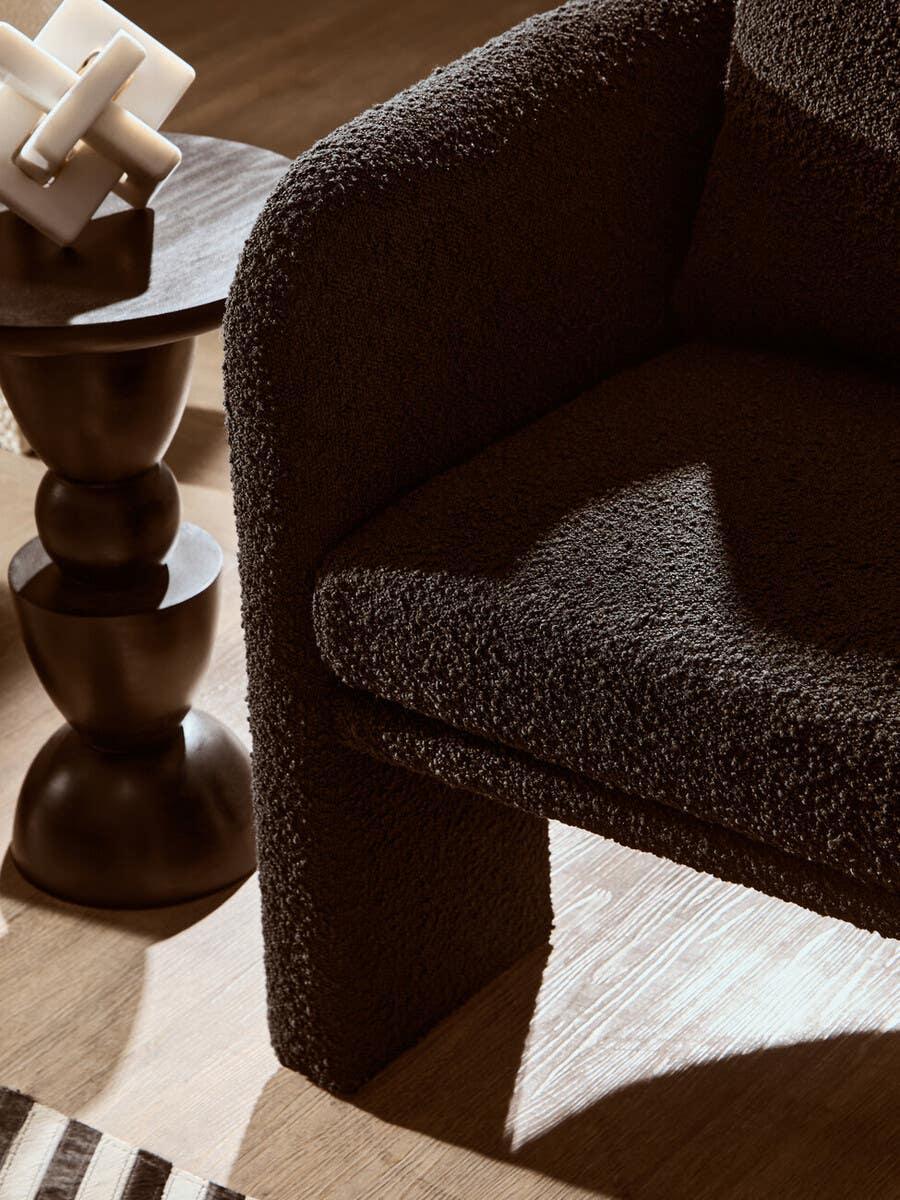 Textured brown armchair beside dark wood side table with modern decor accent
