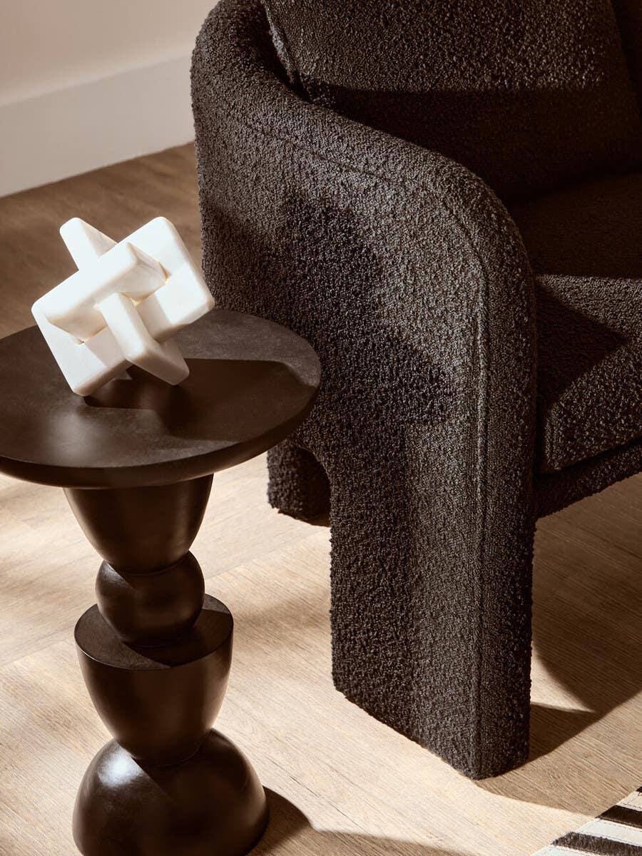 Curved black boucle armchair beside modern dark wood side table with white sculpture